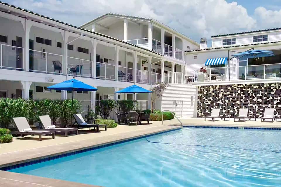 Resort pool with lounge chairs, blue umbrellas, and modern multi-story accommodation buildings