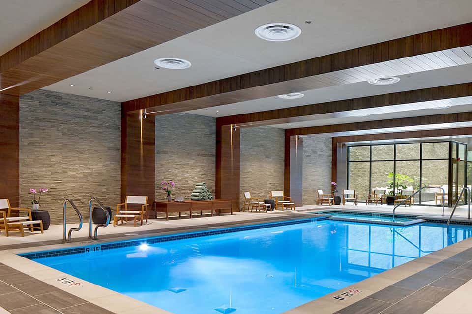 Indoor heated swimming pool with wooden beams, large windows, and comfortable seating area
