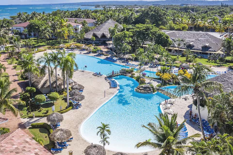 Tropical resort aerial view with multiple pools, palm trees, and thatched roof structures
