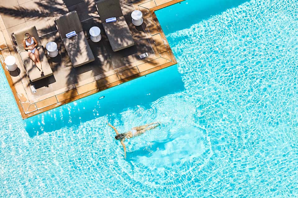Overhead view of guest swimming in turquoise pool near wooden deck and lounge area