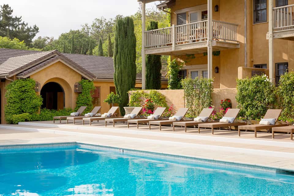 Resort pool surrounded by lounge chairs, Mediterranean villa, and lush landscaping
