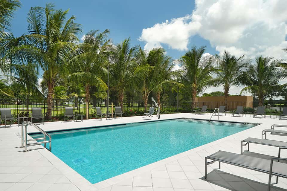 Resort swimming pool with turquoise water, lounge chairs, palm trees, and green landscaping