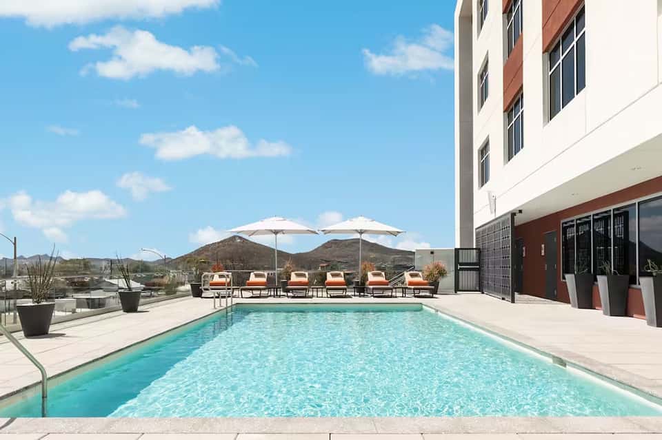 Rooftop pool with mountain views, orange loungers, white umbrellas, and contemporary hotel building