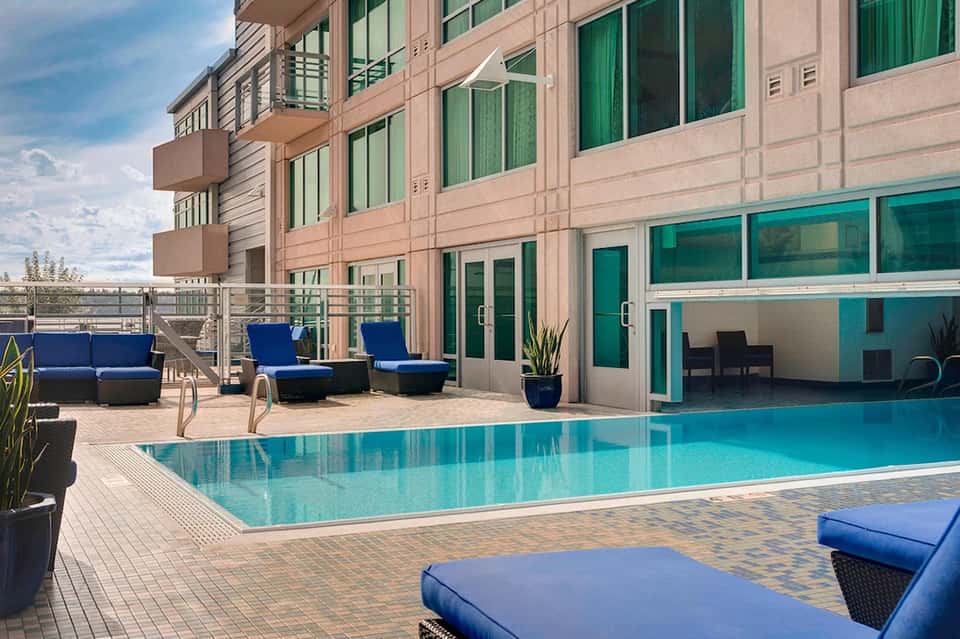 Modern residential building with pool deck, blue lounge seating, and glass patio doors