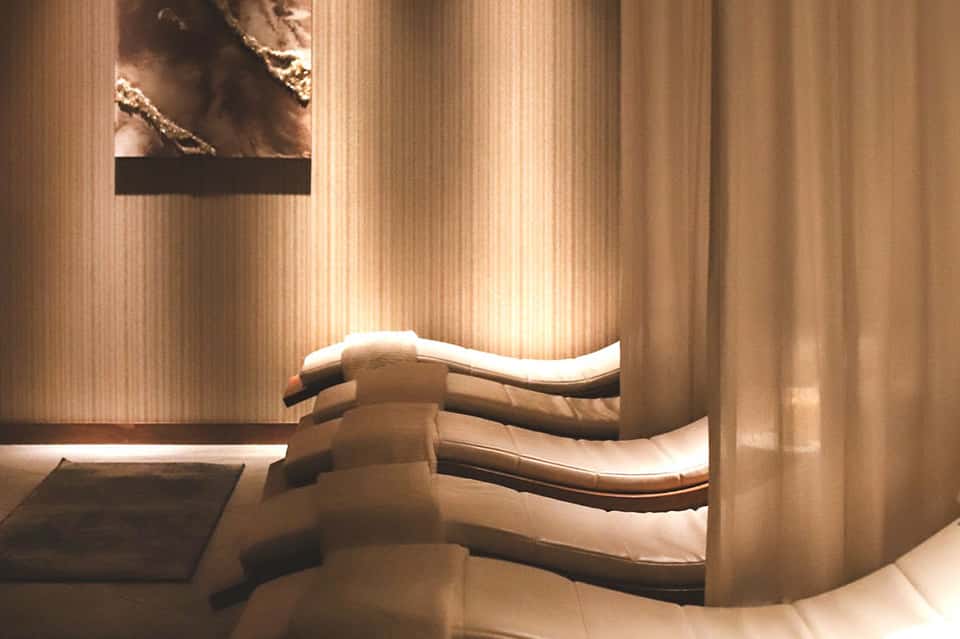 Spa treatment room with curved stone lounges and warm ambient lighting through flowing curtains