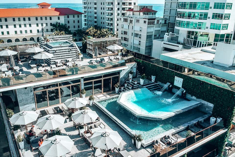 Aerial view of rooftop pool and lounging deck surrounded by beachfront high-rise hotel buildings
