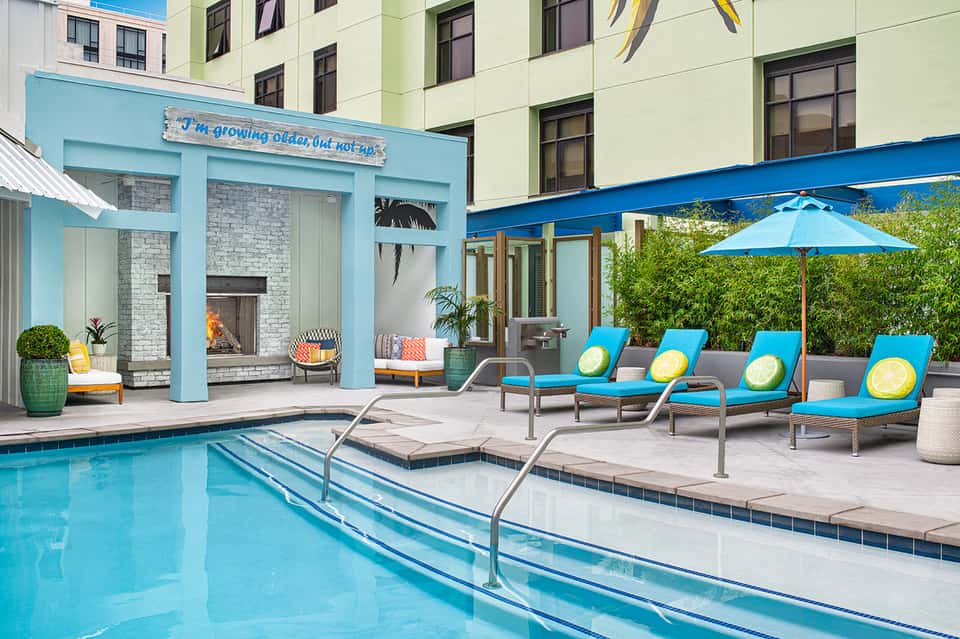 Resort pool with blue lounge chairs, umbrellas, fireplace, and colorful building architecture