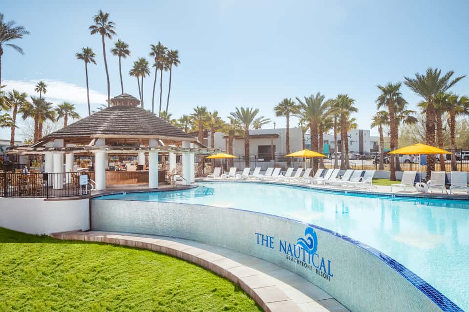 Expansive resort pool with cabana, palm trees, yellow umbrellas, and manicured lawn
