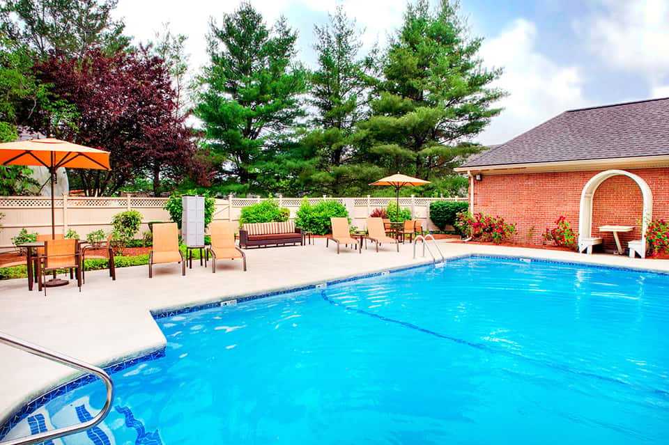 Resort swimming pool with blue water, lounge chairs, umbrellas, and brick building