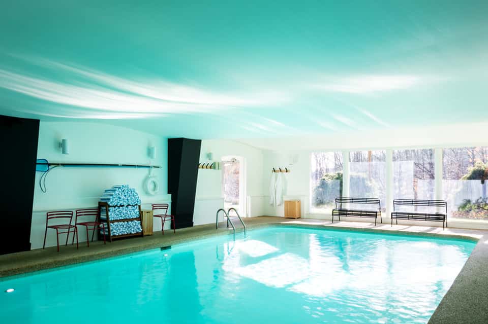 Bright indoor swimming pool with turquoise water and large windows overlooking landscape