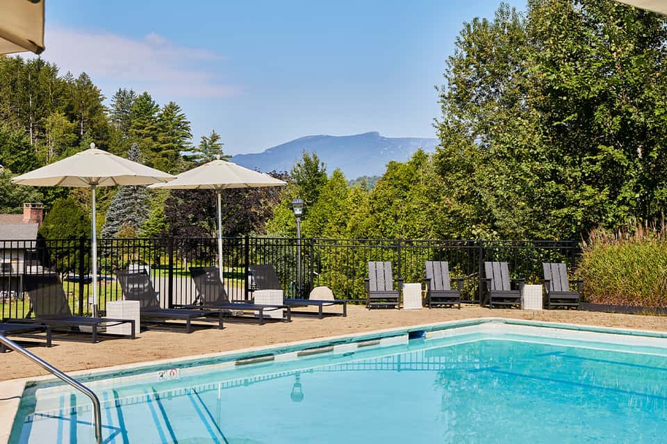Mountain view pool with sandy deck, lounge chairs, umbrellas, and forested landscape