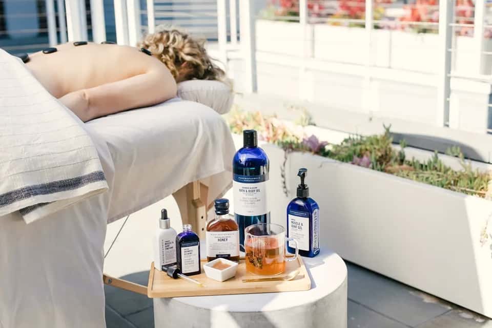 Spa products and honey on table next to person relaxing on lounge chair by pool