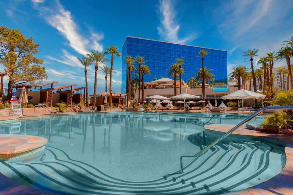 Modern resort pool with geometric tile design, palm trees, and contemporary blue glass building