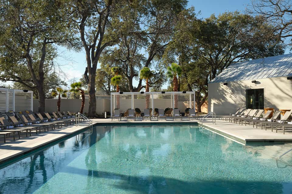 Rectangular resort pool with turquoise water, lounge chairs, and modern poolside buildings with trees