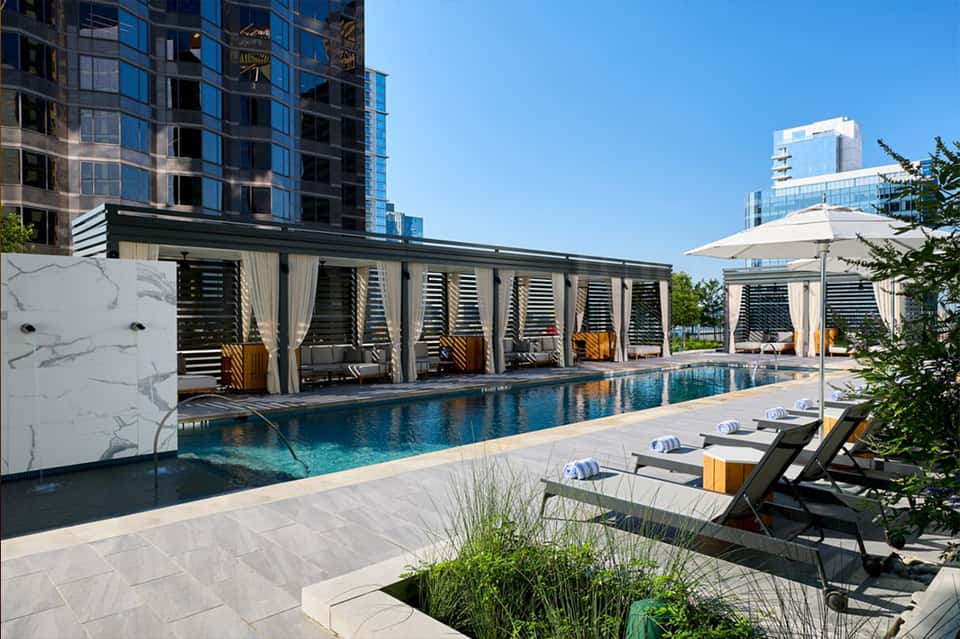 Contemporary rooftop pool with louvered shade structures, modern high-rise buildings, and urban skyline views