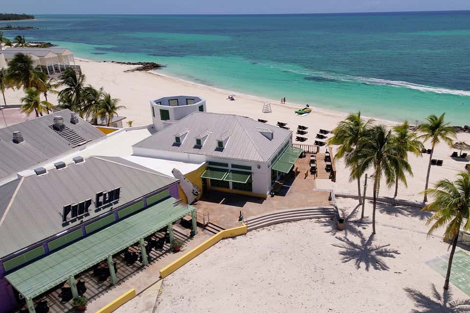 Aerial view of beachfront resort with modern white structures, palm trees, and turquoise ocean waters