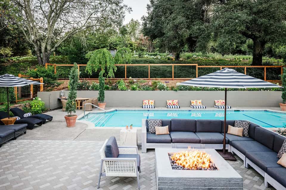 Luxury resort pool area with striped umbrellas, fire pit seating, and manicured gardens behind metal fencing