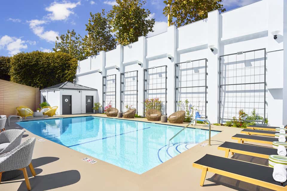 Resort pool with yellow lounge chairs, white pergola structures, and landscaped gardens under blue sky