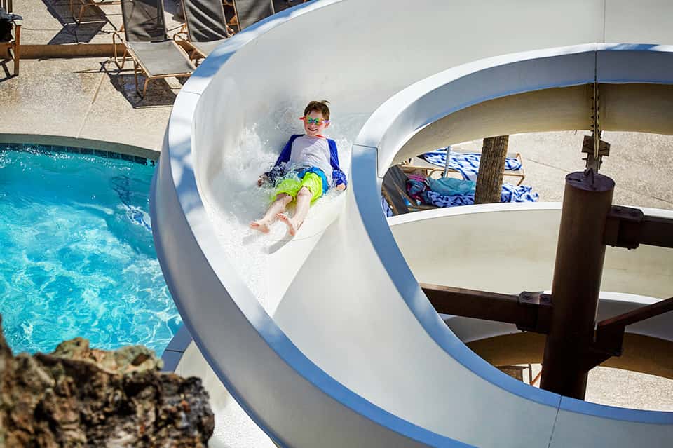 Child sliding down white water slide into turquoise pool at resort