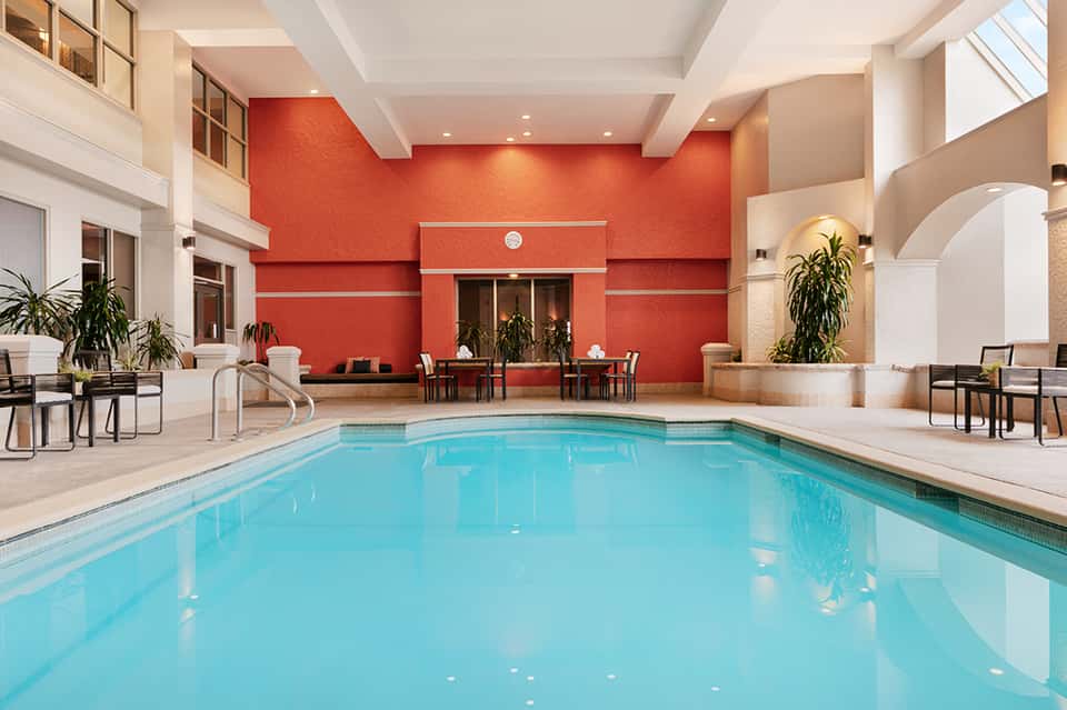 Indoor hotel swimming pool with bright turquoise water, red accent wall, and modern architectural design