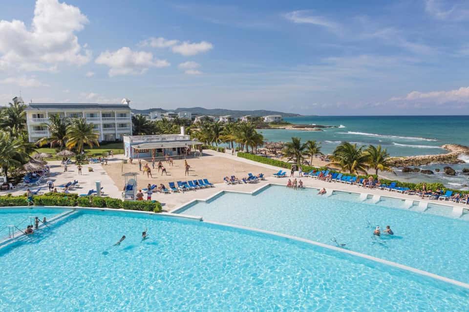 Beachfront resort with multiple pools, palm trees, and ocean view with sandy beach and lounge chairs