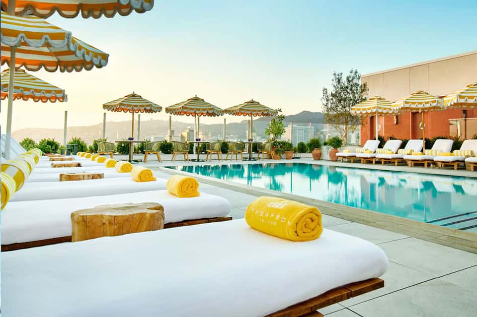 Luxury rooftop pool with yellow umbrellas, white loungers, and city skyline view
