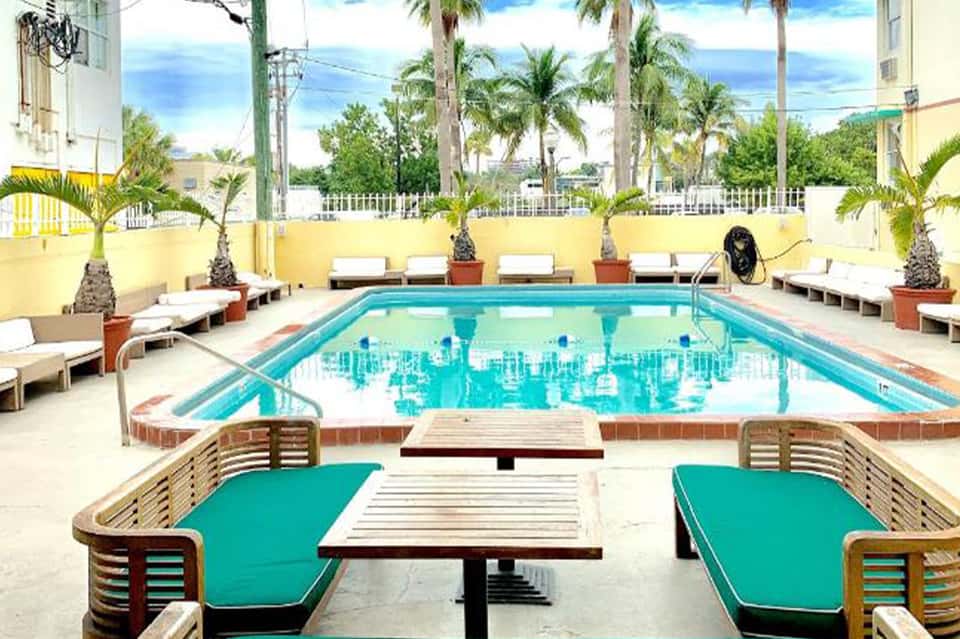 Bright yellow-walled courtyard with rectangular turquoise swimming pool, lounge chairs, and palm trees