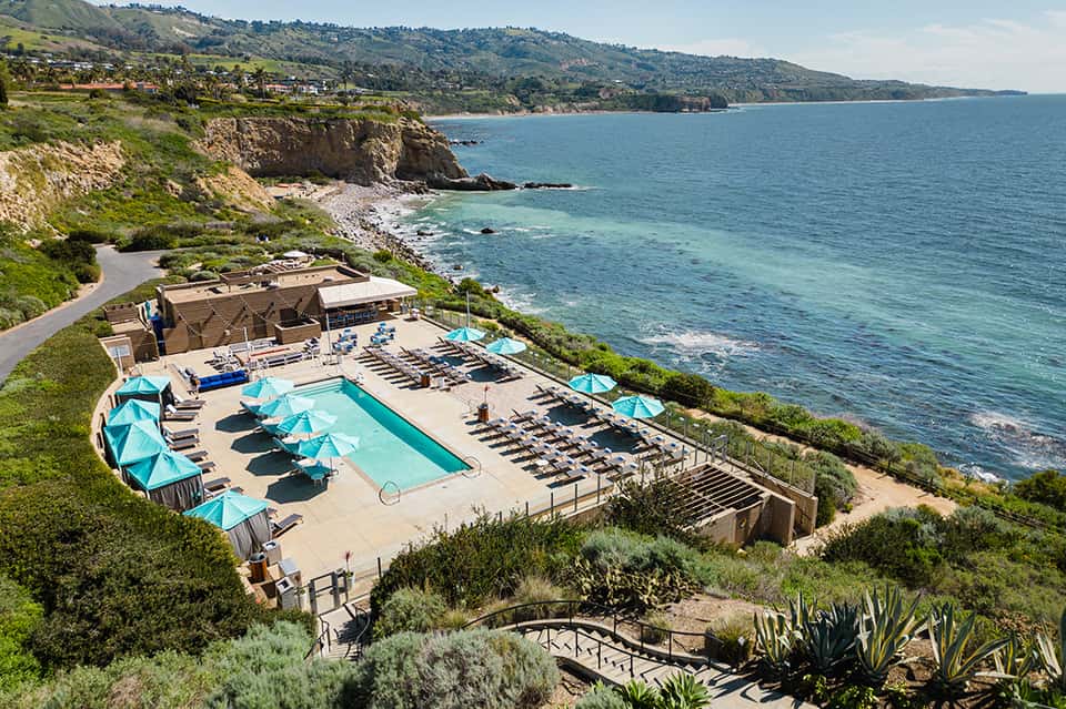 Clifftop resort pool with turquoise umbrellas overlooking coastal landscape