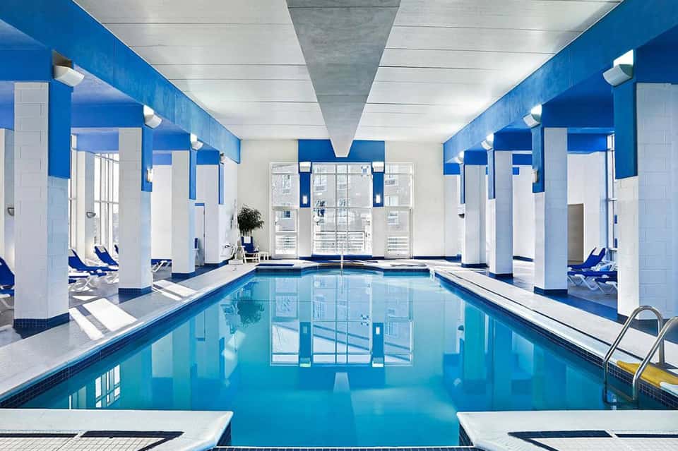 Indoor lap pool with blue and white striped walls, white columns, and lounge chairs