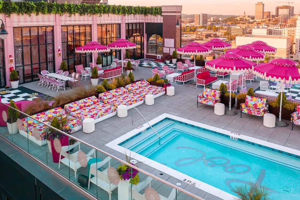 Rooftop pool area with vibrant pink umbrellas, lounge chairs, colorful cushions, and pink building facade