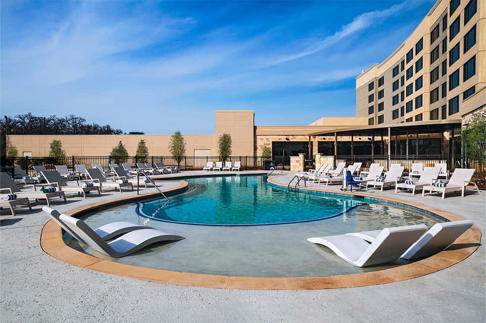 Contemporary hotel pool with lounge chairs, umbrellas, and multi-story building backdrop