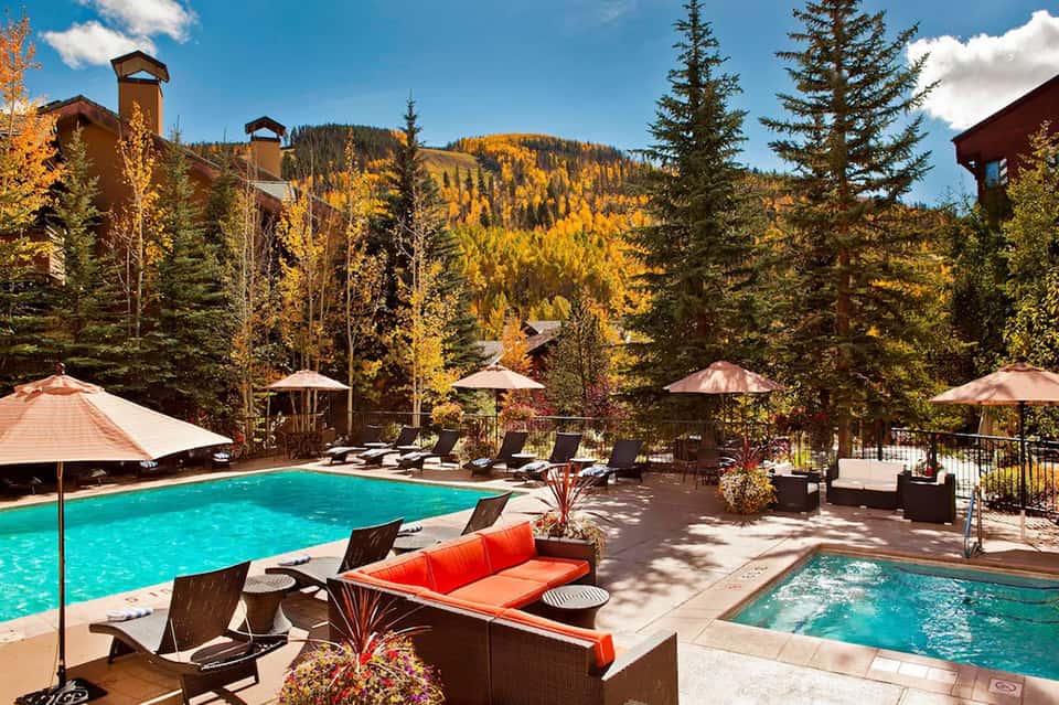 Mountain resort pool with golden aspen trees, lounge chairs, umbrellas, and rustic lodge buildings in autumn