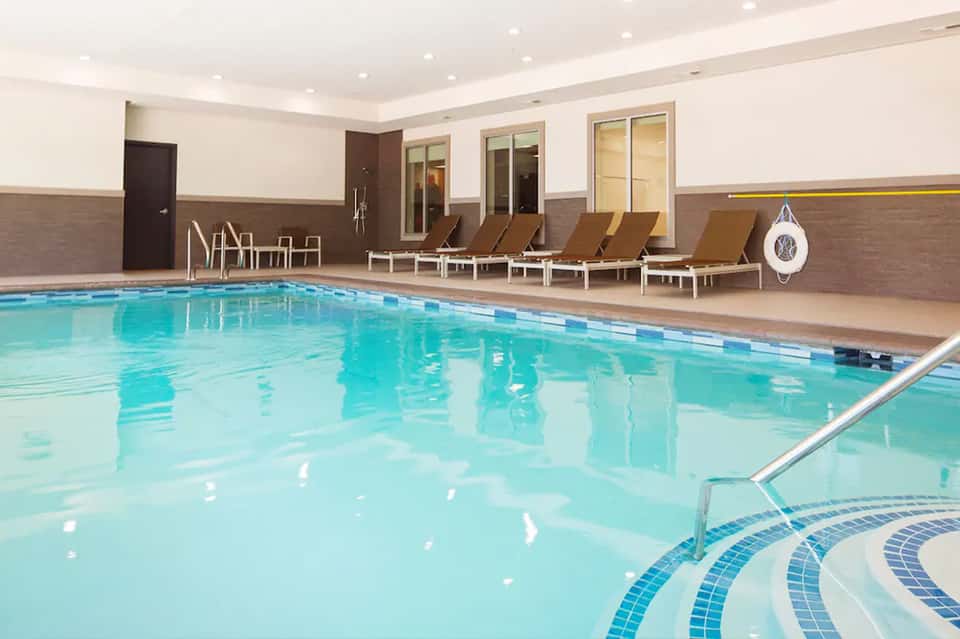 Indoor swimming pool with lane markings, lounge chairs, and floor-to-ceiling windows in a modern facility