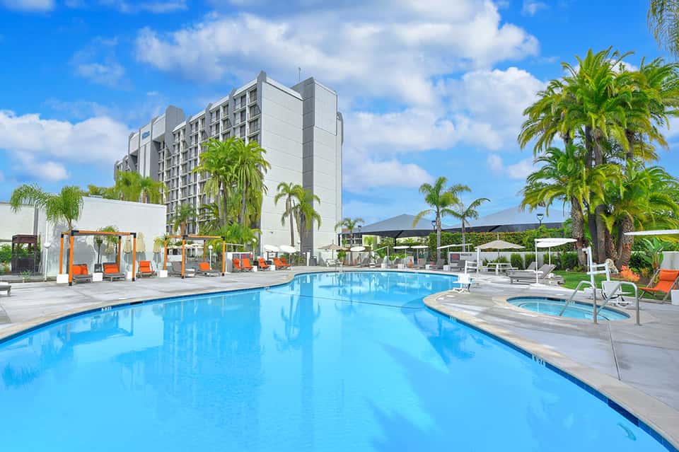 Resort pool with loungers and palm trees, modern high-rise building under blue sky