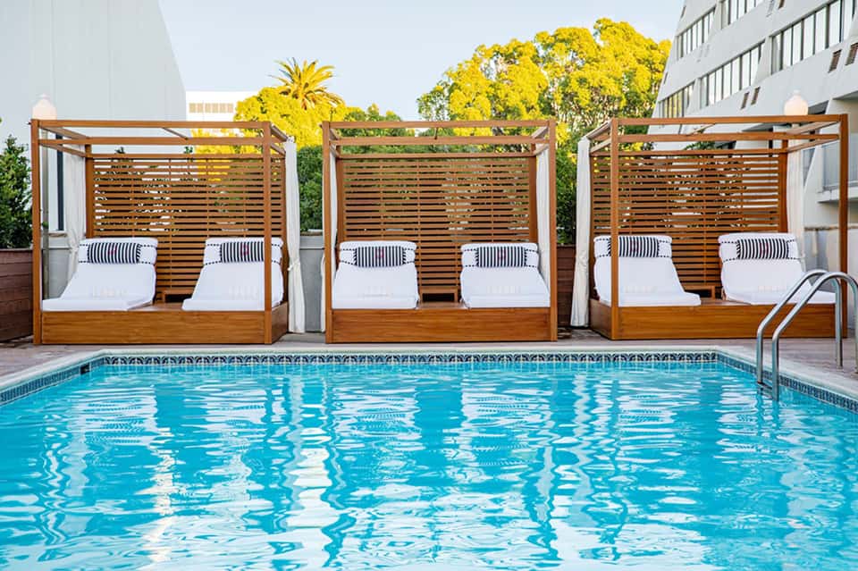 Luxury pool cabanas with wooden frames, white bedding, and turquoise swimming pool