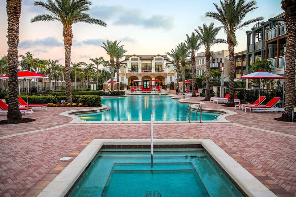 Resort pool area with red umbrellas, spa building, and palm trees in tropical setting