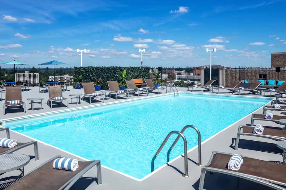 Rooftop pool with bright blue water, lounge chairs, and city skyline views under clear blue sky