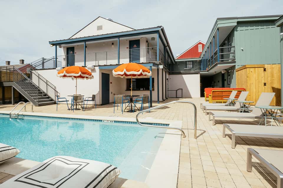 Beachfront resort pool with orange umbrellas, modern clubhouse, and waterfront lounge chairs