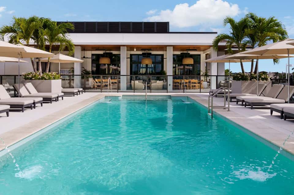 Modern resort pool with turquoise water, loungers, umbrellas, and contemporary building with palm trees
