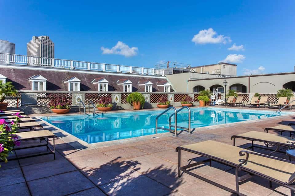 Rooftop pool with lounge chairs, decorative planters, and city skyline views under blue sky