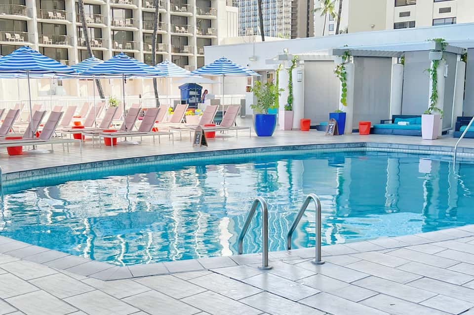 Resort pool with blue and white striped umbrellas, lounge chairs, and residential buildings in the background