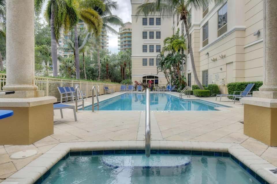 Luxurious resort pool with spa jet in foreground, surrounded by tall palm trees and multi-story hotel buildings