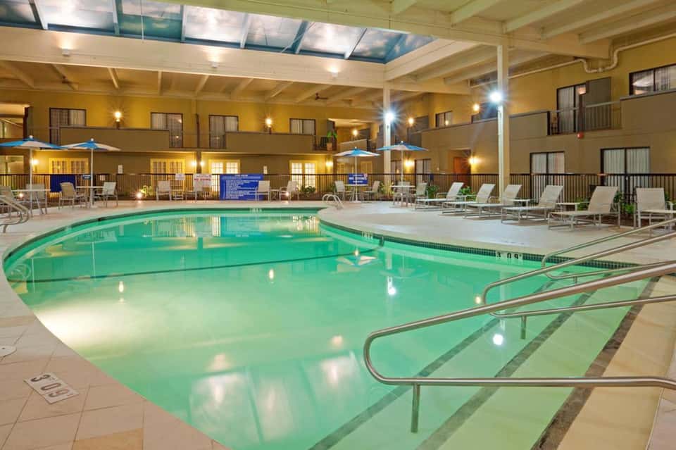 Indoor pool with turquoise water, lounge chairs, and multi-level hotel building with skylights