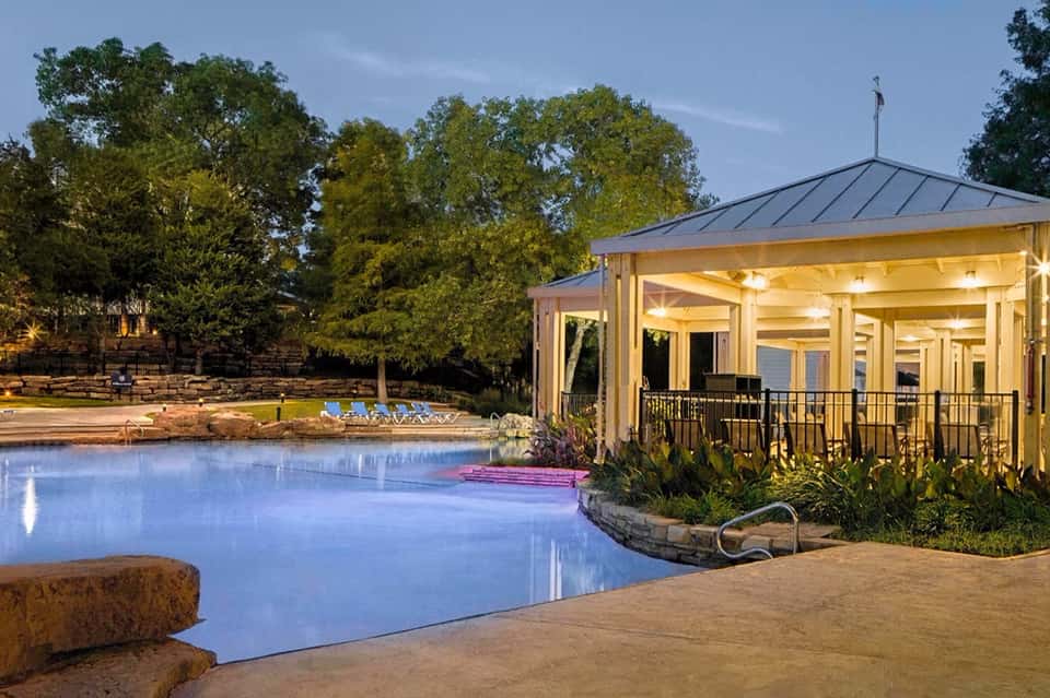 Illuminated pool house at dusk with manicured grounds and fire pit seating area