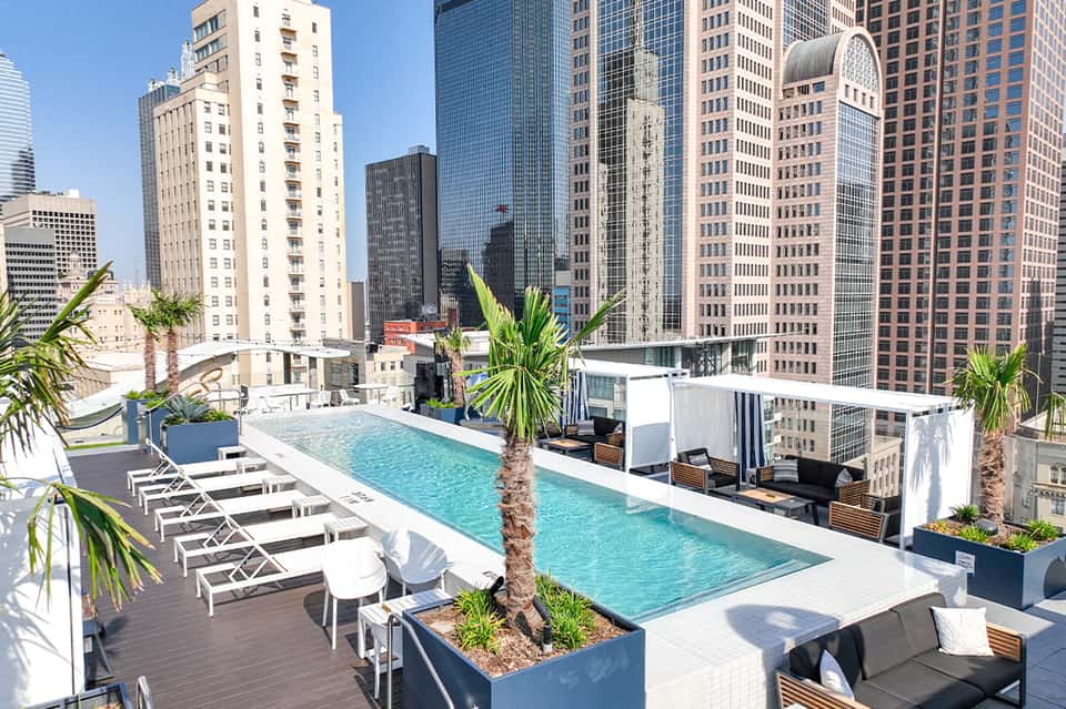 Rooftop pool with lounge chairs overlooking downtown cityscape and tall buildings