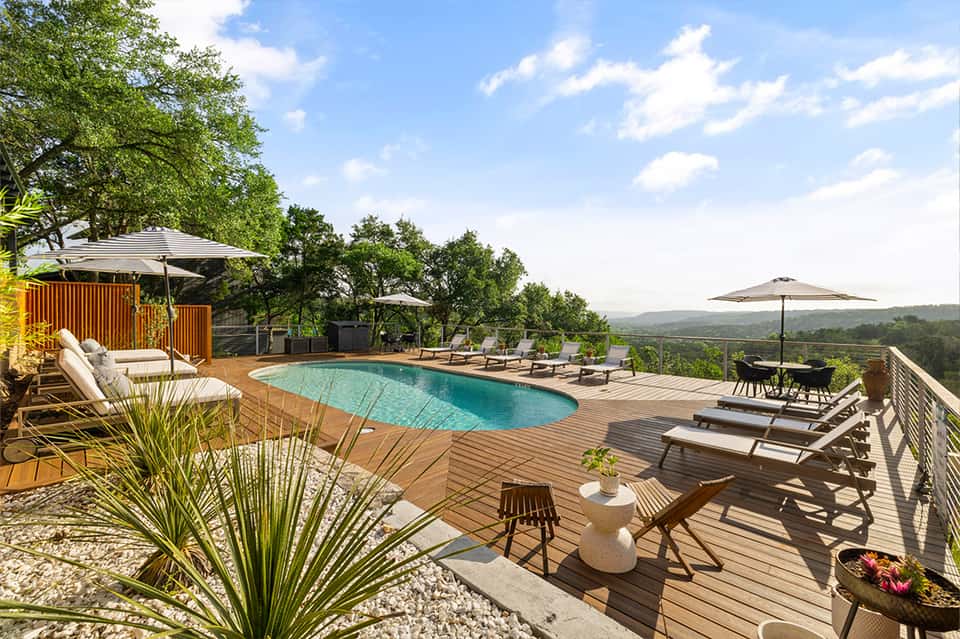 Resort pool deck with lounge chairs, umbrellas, and scenic hillside views surrounded by trees