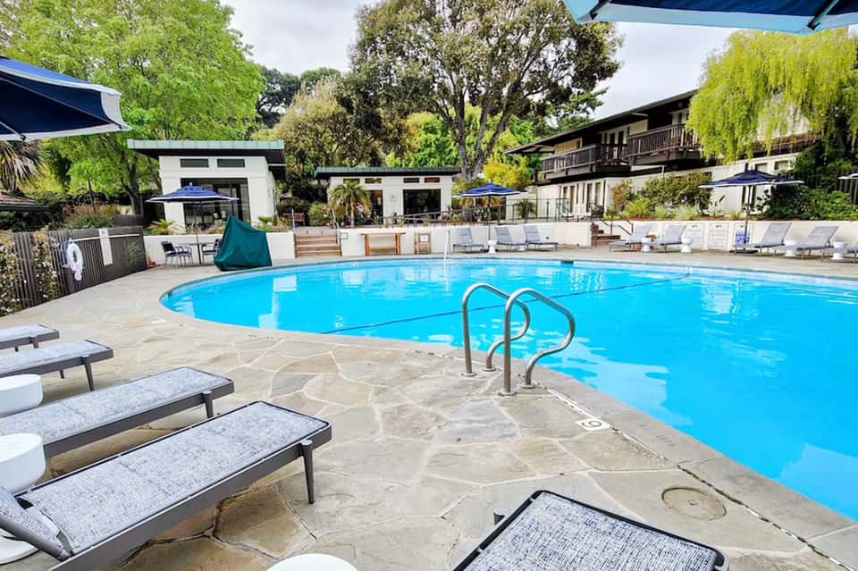 Resort swimming pool with lounge chairs, lush green landscaping, and modern building structures