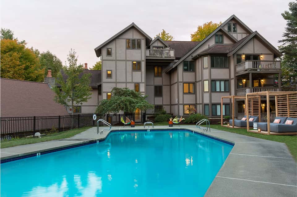 Modern Tudor-style residential building with pool, lounge chairs, and wooden pergola in autumn setting