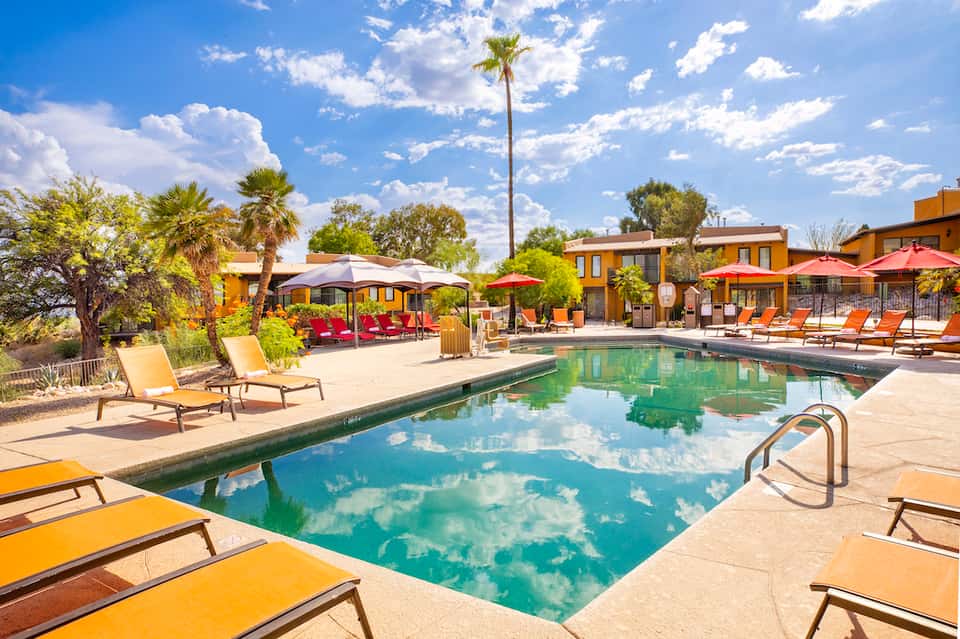 Resort pool area with yellow loungers, palm trees, and yellow umbrellas under clear blue sky