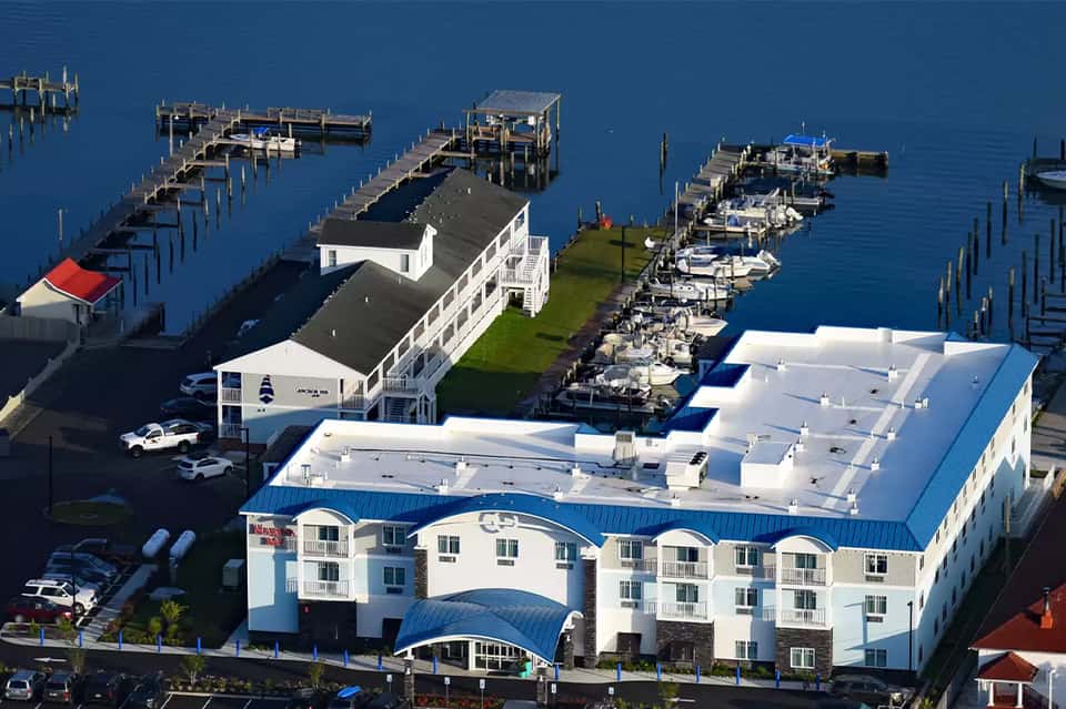 Aerial view of waterfront resort with white building, boat docks, and blue water